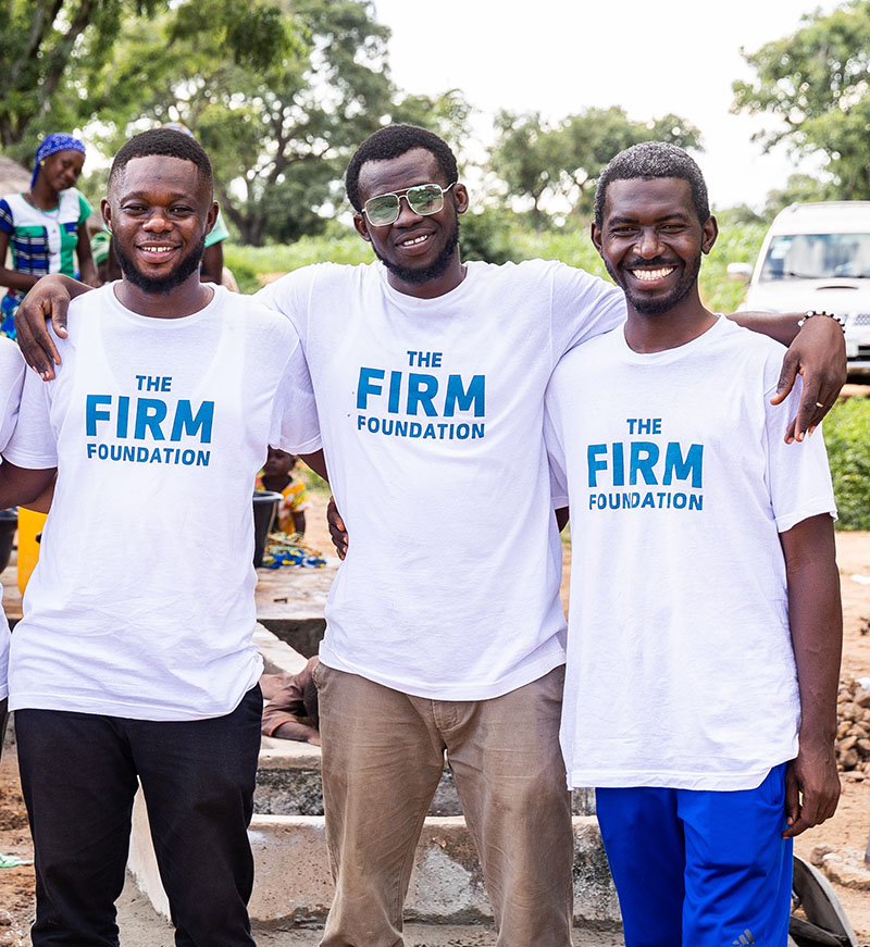 Three of the Community Impact Leaders in Ghana smiling for the camera. Wearing white shirts that say The Firm Foundation