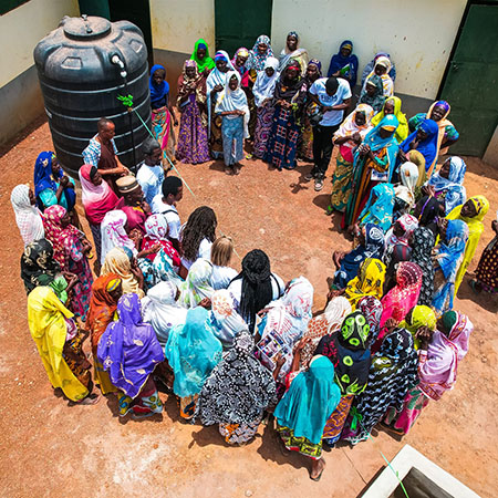A circle of women standing in front of a water container